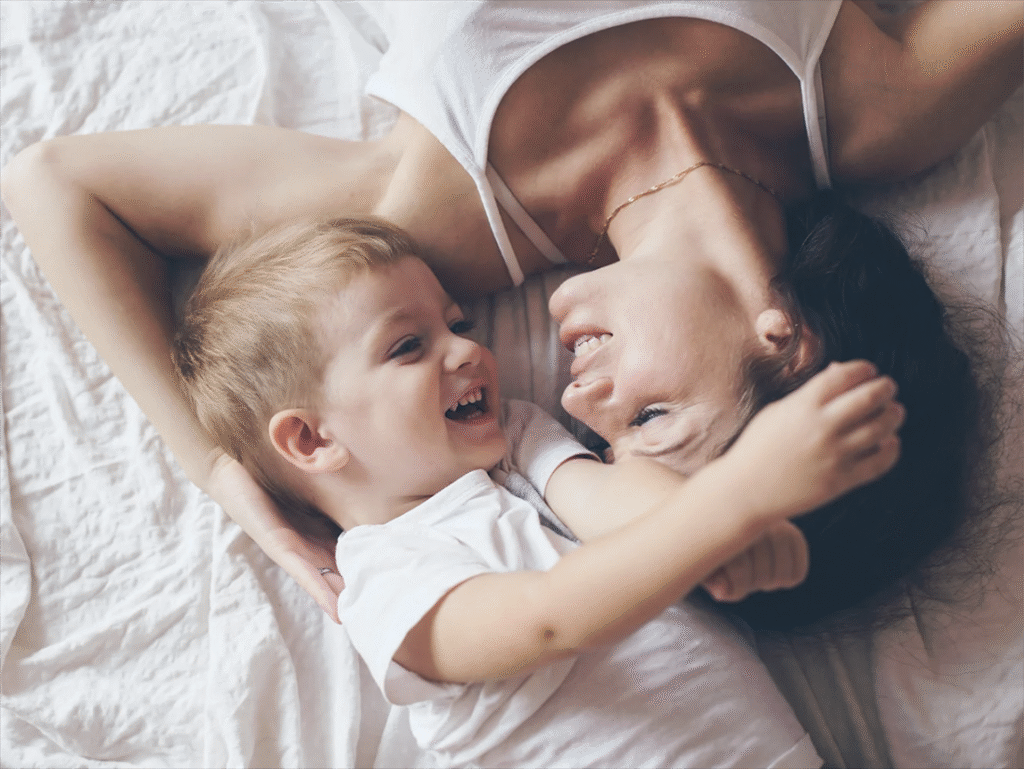Young child and mother laughing together in bed, enjoying a playful moment