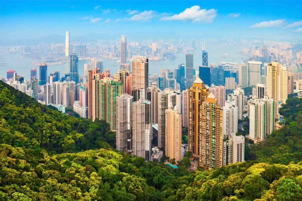 Panoramic view of the Hong Kong skyline from Victoria Peak at sunset, with skyscrapers, harbor, and mountains in the background.