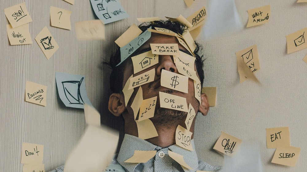Image of a man with many post it's illustrating the stress of overload of tasks